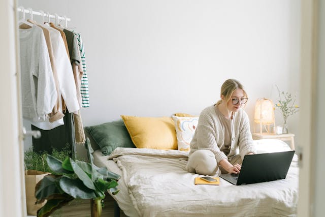 woman sitting on a bed while using a laptop